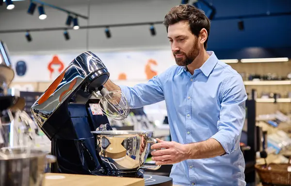 Bir adam, perakende mağazası için tasarlanmış ve potansiyel alıcılara çeşitli özelliklerini, işlevlerini ve parlak tasarımlarını gösteren çağdaş bir stand mikserle meşgul oluyor.