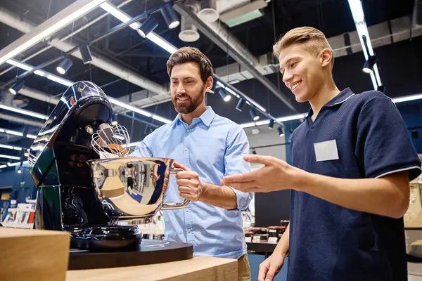 Bir müşteri, canlı bir perakende satış ortamı ile çevrili iken, bir prim standı mikserinin özelliklerini ve faydalarını keşfetmek için, bilgili bir satış danışmanıyla aktif bir şekilde sohbet eder.