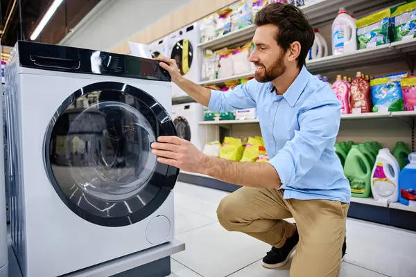 Müşteri, çeşitli çamaşır deterjanı seçenekleri ve sayısız temizlik ürünleriyle çevrili bir mağaza koridorunda bulunan şık ve modern bir çamaşır makinesini dikkatle inceliyor.