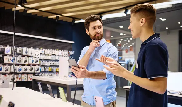 Modern bir perakende satış ortamında, müşteri en son akıllı telefonlar hakkında bilgili bir satıcıya hevesle konuşur ve etkileşim sırasında kişiselleştirilmiş servisin değerini vurgular.