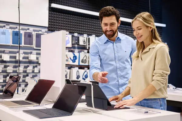 Çağdaş bir teknoloji mağazasında, arkadaş canlısı ve bilgili bir perakende temsilcisi müşteriye çeşitli ürünleri sergileyerek yardımcı olurken, aynı zamanda değerli rehberlik ve içgörü sunmaktadır.