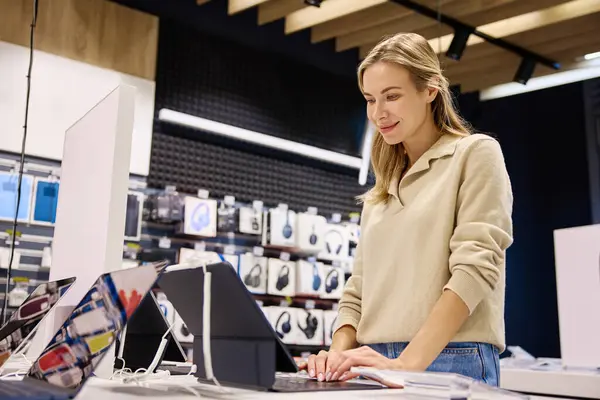 Şık, çağdaş bir perakende mağazasında, genç bir kadın çeşitli elektronik cihazlarla derinden ilgilenerek, bu sahneyi teknoloji perakendecileri ve modern yaşam tarzını gösteren görüntüler için mükemmel hale getiriyor.