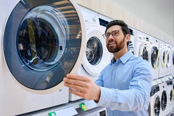 Bugünün modern perakende alışverişinin karmaşıklığını ve zorluklarını vurgulayan çeşitli seçenekleri ve fiyatları düşünceli bir şekilde tartan bir adam bir dizi çamaşır makinesinin önünde duruyor.