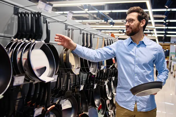 Bir adam, mutfak malzemesi satan bir mağazada sergilenen tavayı dikkatle inceliyor. Bu tavada, mutfak deneyimlerini geliştirmek için çeşitli mutfak gereçleri ve mutfak malzemesi seçenekleri sunuluyor.