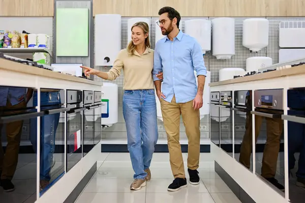 Genç bir çift, mutfak aletlerini bir mağazada keşfediyor, seçenekleri tartışıyor ve keyifli deneyimleri birlikte kutluyor, düşünceli seçimler yoluyla bağlarını güçlendiriyor.