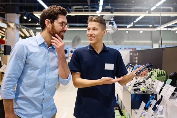 Çağdaş bir perakende satış ortamında, bir müşteri bir mağaza çalışanı ile alışverişe hazır çeşitli elektronik cihazları araştırırken sohbet eder.