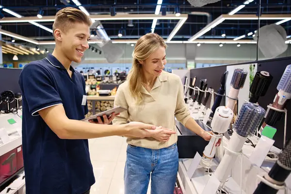 Parlak, modern bir mağaza ortamında bilgili bir satıcıyla saç şekillendirme aletlerini keşfeden mutlu bir müşteri.