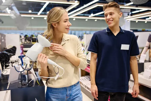 Parlak, modern bir mağaza ortamında bilgili bir satıcıyla saç şekillendirme aletlerini keşfeden mutlu bir müşteri.