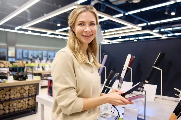 Genç bir kadın, modern ve şık bir perakende mağazasından uygun bir saç düzleştirici seçerken neşeli bir şekilde gülümsüyor. Etrafı canlı stil araçları ve modaya uygun dekorlarla çevrili.