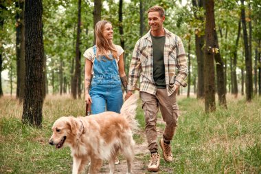 Neşeli bir çift, güzel, yemyeşil bir ormanda el ele dolaşır. Çevrelerindeki büyüleyici güzelliğin tadını çıkarırken büyüleyici Golden Retriever 'larıyla birlikte mutlu mesut dolaşırlar.
