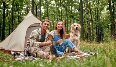 Neşeli bir çift, doğanın güzelliğinin tadını çıkarırken ve ormanın derinliklerinde sunduğu rahatlığı kucaklarken neşeli Golden Retriever 'larıyla harika bir kamp gezisinin tadını çıkarıyor.