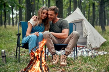 Sevgi dolu bir çift, kamp ateşinin yanında, huzurlu bir akşamın huzurlu atmosferinin tadını çıkarıyor. Romantizmin ve dışarıda, yıldızların altında keşfe çıkmanın heyecanı.