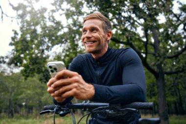 Neşeli bir bisikletçi, canlı bir açık havada, akıllı telefon kullanarak, spor, teknoloji ve eğlenceyi harmanlayarak, doğal güzellikler arasında ferahlatıcı bir eğlence ve keşif deneyimi yaratıyor.