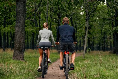 Sevgi dolu bir çift, uzun, görkemli ağaçlar ve etraflarındaki doğanın huzur verici sükuneti ile çevrili, büyüleyici, güzel yeşil bir ormanda mutlu ve huzurlu bir bisiklet yolculuğunun tadını çıkarır.