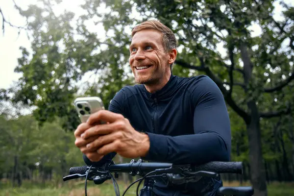 Neşeli bir bisikletçi, canlı bir açık havada, akıllı telefon kullanarak, spor, teknoloji ve eğlenceyi harmanlayarak, doğal güzellikler arasında ferahlatıcı bir eğlence ve keşif deneyimi yaratıyor.