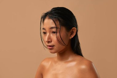 Parlak tenli Asyalı kadın bej arka planda yalnız poz veriyor. Cilt bakımı, kozmetoloji ve kaplıca tedavisi kavramı.