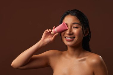 Esmer arka planda temiz, pırıl pırıl bir cilt temeli ya da kremi olan Asyalı çekici kadın. Kozmetik, cilt bakımı ve makyaj kavramı.