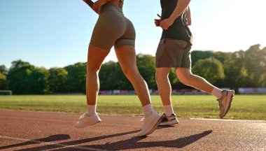 Genç ve zinde bir çift sabahleyin stadyum pistinde birlikte koşuyor. Sağlıklı yaşam tarzı, motivasyon ve güneş ışığı rutin konsepti.