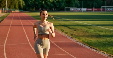 Spor giyimli genç bir bayan gün batımında stadyum pistinde koşuyor. Zindelik, kararlılık ve aktif yaşam tarzı kavramı.