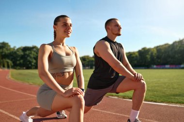 Atletik erkek ve kadın stadyum pistinde hamlesini yapıyor. Sabah egzersizi, esneme hareketleri ve sağlıklı yaşam tarzı konsepti..