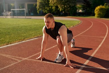 Formda genç bir adam gün doğumunda açık hava pistinde koşmaya hazırlanıyor. Odaklanmış ve kararlı ifade. Disiplin, hız ve sağlıklı yaşam tarzı kavramı.
