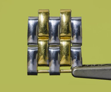 Metalik bir saat bileziğinin gümüş ve altın renkli halkalarının yanında.