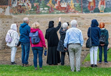 Rahibe, turistlere Romanya 'nın Bukovina kentindeki Sucevita manastırının ortodoks kilisesinin dış duvarlarındaki freski açıklıyor.