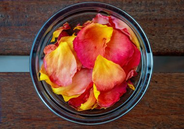 Kurumuş kırmızı ve sarı gül yapraklı cam kâse ile süslenmiş bir masa.