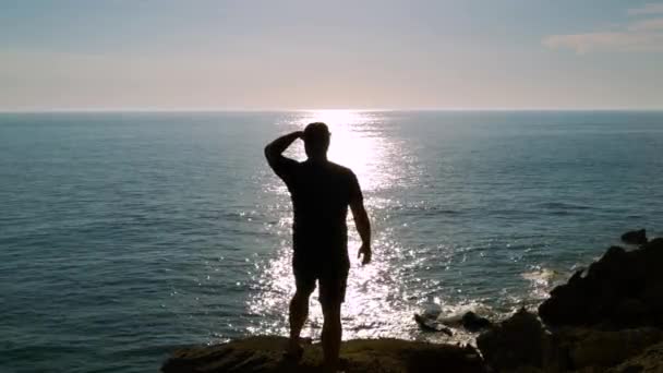 一个人在悬崖上的轮廓 背景是阳光在海水上反射的痕迹 形成了概念 — 图库视频影像