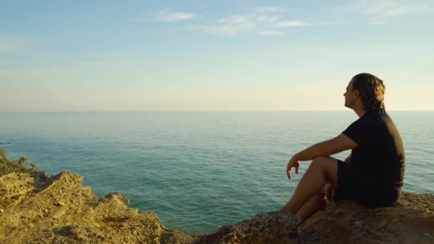 Человек Сидит Скале Пляже Морской Водой Заднем Плане Голубым Небом — стоковое видео