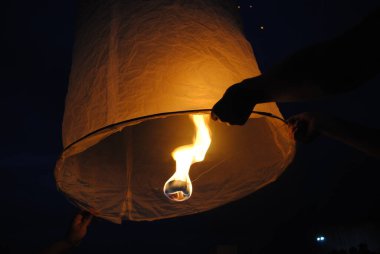 Gece gökyüzü feneri fırlatılıyor, eller onu tutuyor ve içinde parlak bir ateş parlıyor..