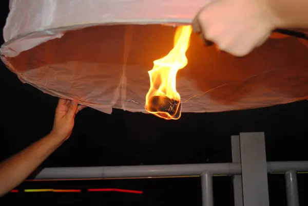 Gece gökyüzü feneri fırlatılıyor, eller onu tutuyor ve içinde parlak bir ateş parlıyor..