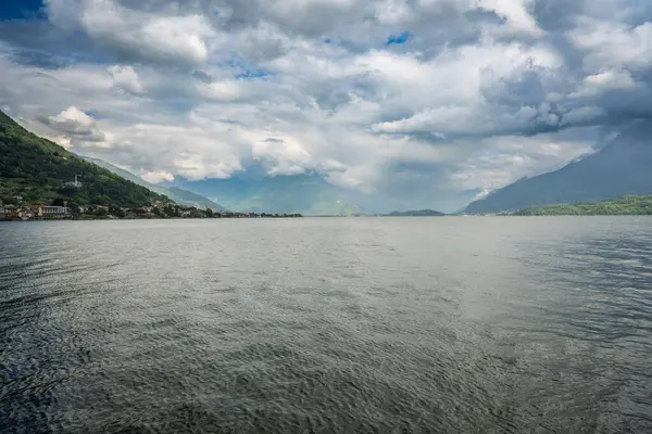 Dramatik bulutlu gökyüzünün altında manzaralı dağ manzarası. Sisli tepeleri, derin suları ve fırtına bulutlarını aşan güneş ışığıyla karamsar bir manzara. Doğa, seyahat ve hava durumu için ideal.