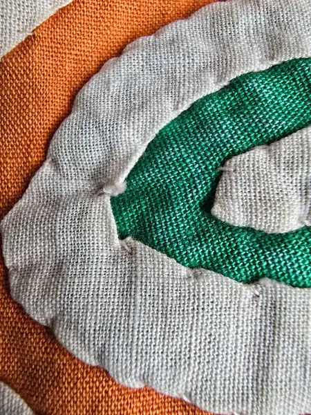 Turuncu, sarı ve yeşil desenli beyaz kumaş arkaplanda soyut sarmal şekilli el yapımı tekstil sanatının yakın çekimi.