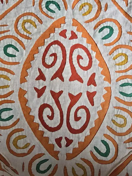 Turuncu, sarı ve yeşil desenli beyaz kumaş arkaplanda soyut sarmal şekilli el yapımı tekstil sanatının yakın çekimi.