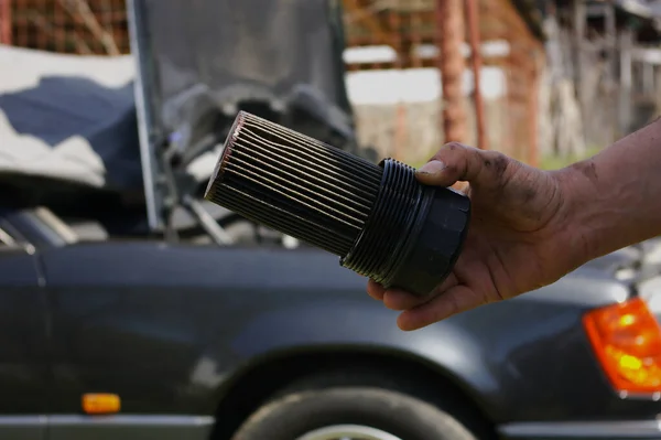 Dirty car oil filter held in a human hand. Used black oil filter designed to remove contaminants from engine, transmission, lubricating, or hydraulic oils.