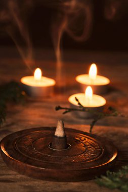 Aromatik tütsü konisi ve dumanı kırsal ahşap masadaki küçük mumlarla çevrili.