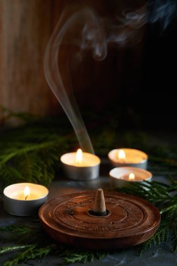 Aromatik tütsü konisi ve dumanının güzelliği küçük mumlarla çevrili dikey bir arka planda.