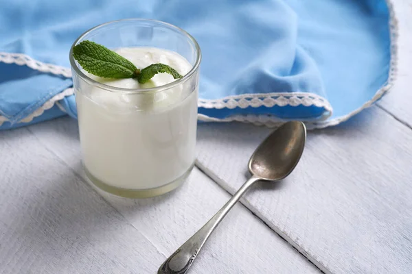 Cam bir kavanozda taze ev yapımı organik yoğurt, içinde nane yaprakları ve kırsal beyaz ahşap bir masada mavi bir peçete.