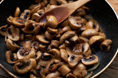 Tavanın içinde soğan olan kızarmış mantarların yakın çekimi.