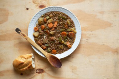 Soğanlı ve havuçlu mercimek tabağı ve rustik masada ekmek, yatay biçimde üst görünüm.