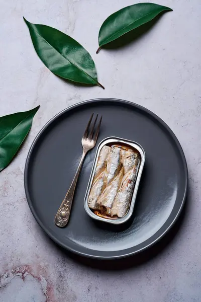 Gri bir tabakta zeytinyağlı sardalya konservesi ve yeşil yapraklar, yukarıdan görünüm