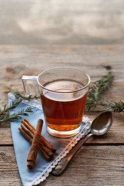 Tarçınlı ve tarçınlı, sade ahşap masa üzerinde siyah çay ve tarçın çubukları olan bir cam bardak.