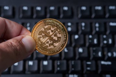 Xrp kripto para birimini tutan bir el klavyenin önünde gösterilir. El klavyenin üstüne yerleştirilir ve Xrp açıkça görülebilir. Bu resim dijital para birimi ve teknoloji entegrasyonu kavramını iletir.