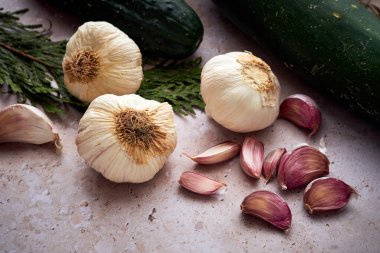 Sarımsak karanfilleri ve soğanlar tezgahın üstüne bırakılmış ve arka planda yeşil bir salatalık var..