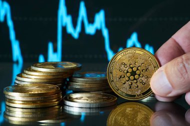 Bulanık bir borsa tablosunun önünde Cardano sikkesini tutan bir el..