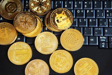 Siyah dizüstü bilgisayara saçılmış altın renkli kripto paralar..
