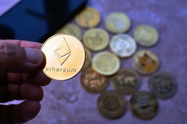 Arka planda farklı madeni paralar bulanıklaşırken, bir el Ethereum şifreleme sikkesini odakta tutar..