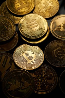 Karanlık bir yüzeyde sanatsal olarak düzenlenmiş çeşitli altın kripto para birimleri..