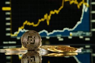 Parlak bir yüzeyde daha fazla madeni para ile çevrili Binance kripto para birimine yakın plan, arka planda yukarı doğru bir pazar eğilimi gösterilmiştir.